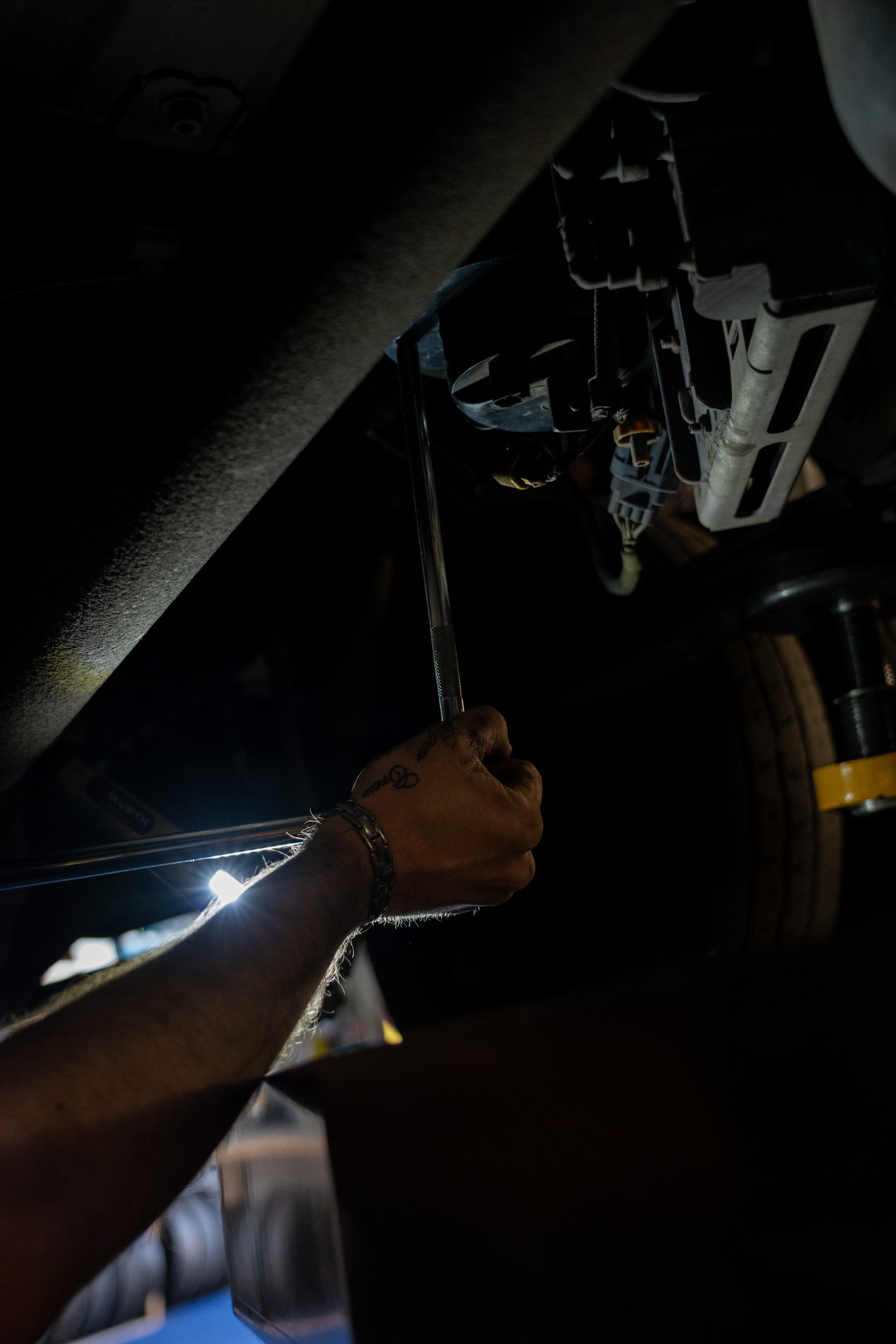 A technician inspecting brakes and suspension under a vehicle by work light