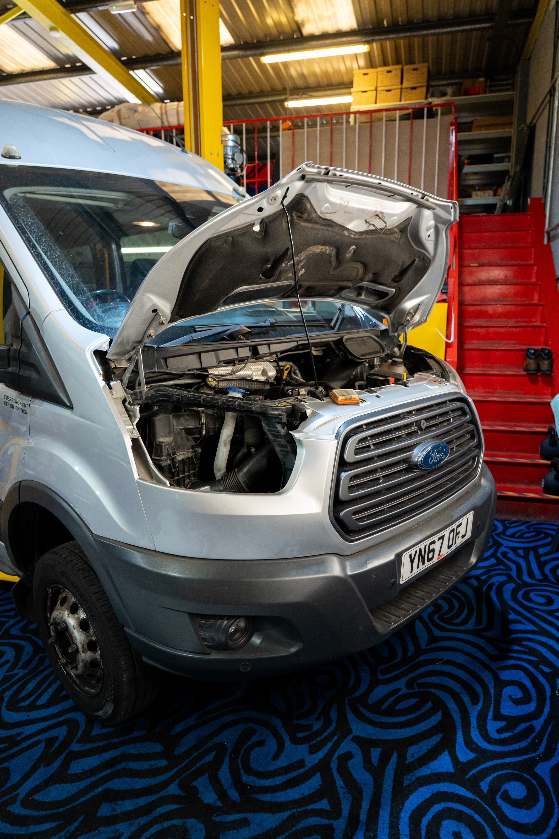 A Ford Transit with its bonnet up being serviced in the workshop